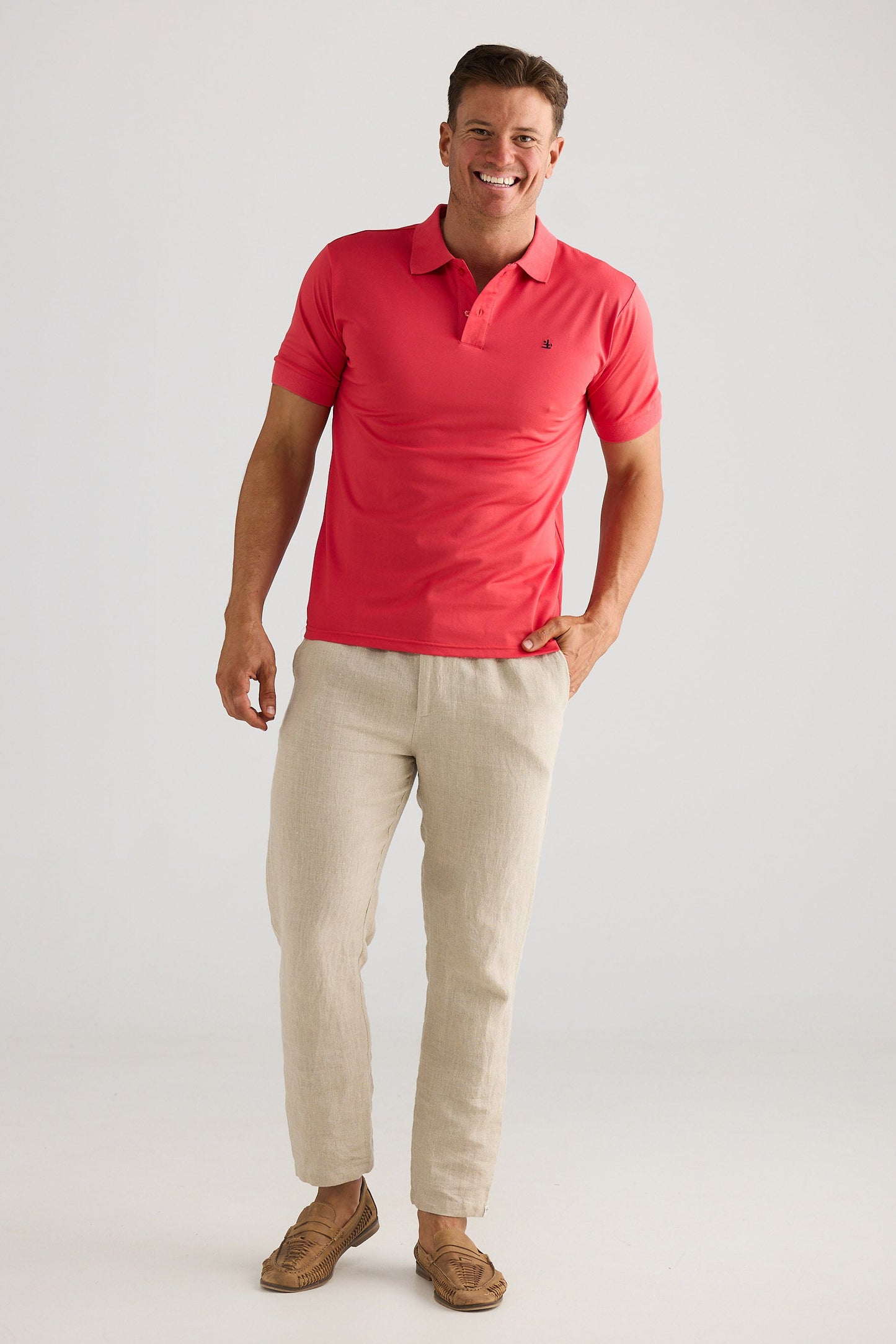 Man wearing a red polo shirt and beige pants on a white background