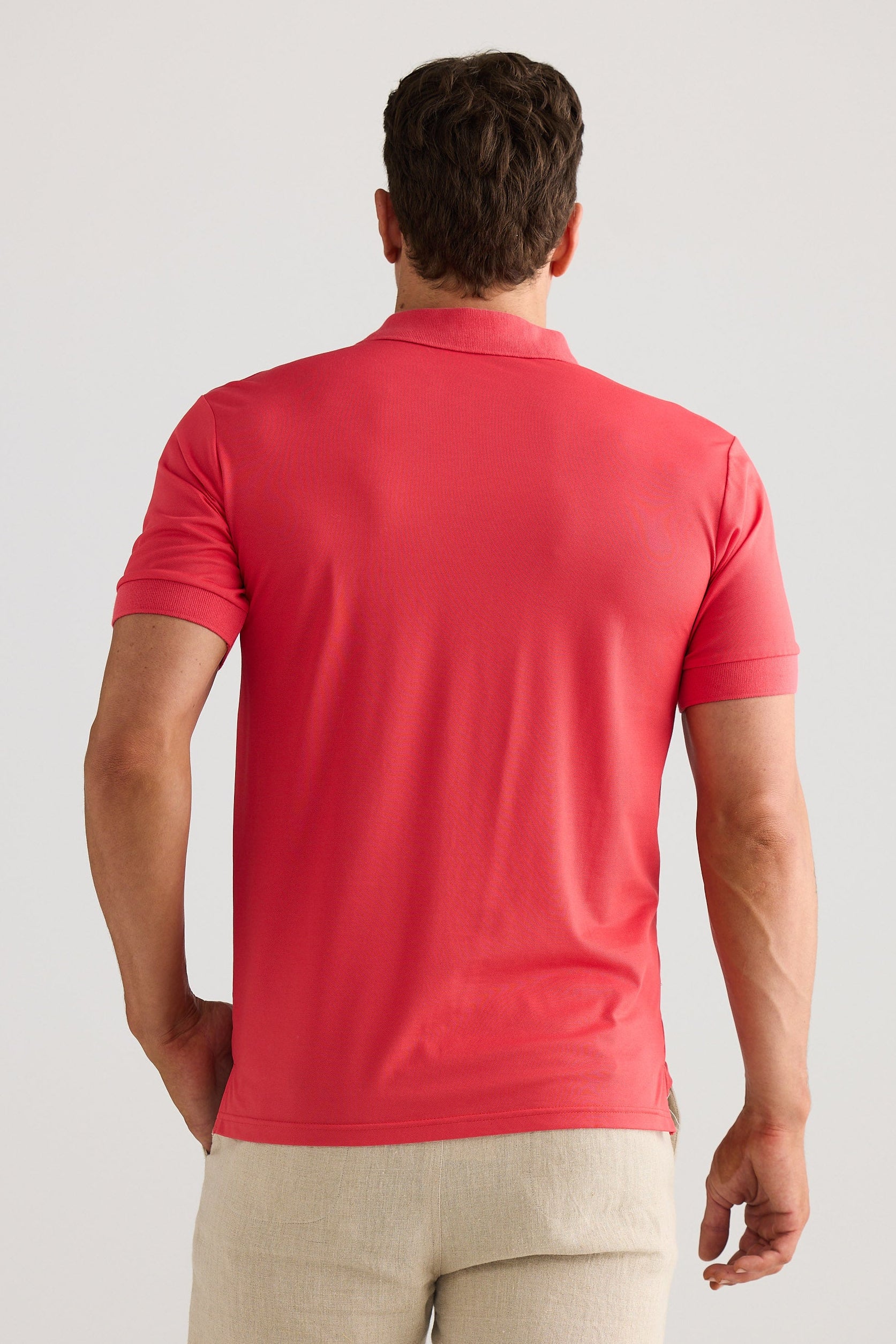 Man wearing a red polo shirt and beige pants against a light gray background