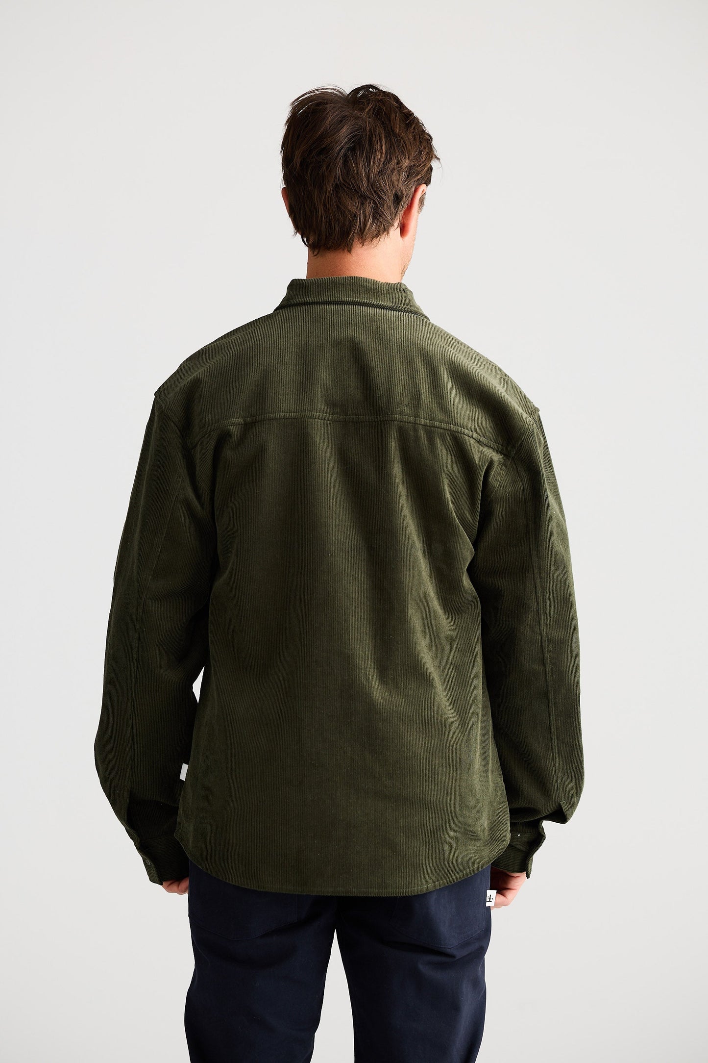 Person wearing a green jacket and dark pants on a white background