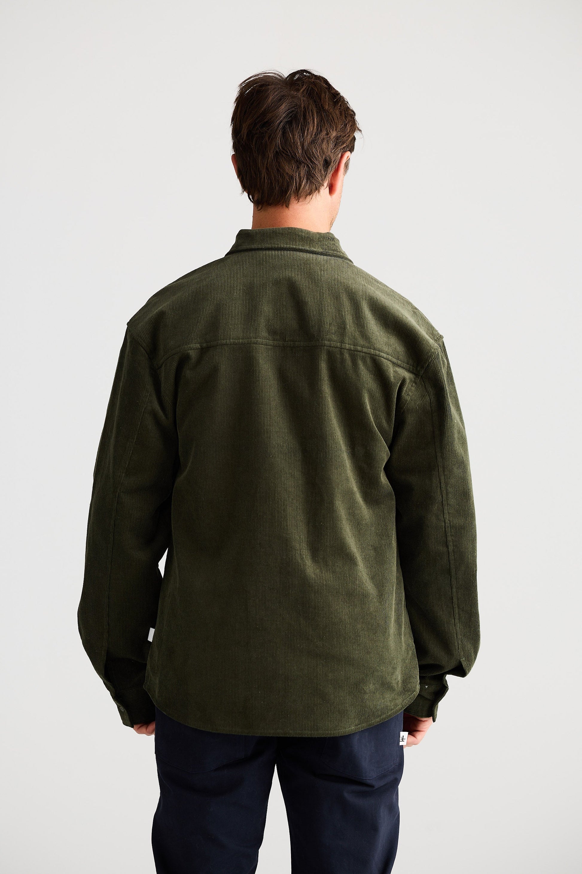 Person wearing a green jacket and dark pants on a white background