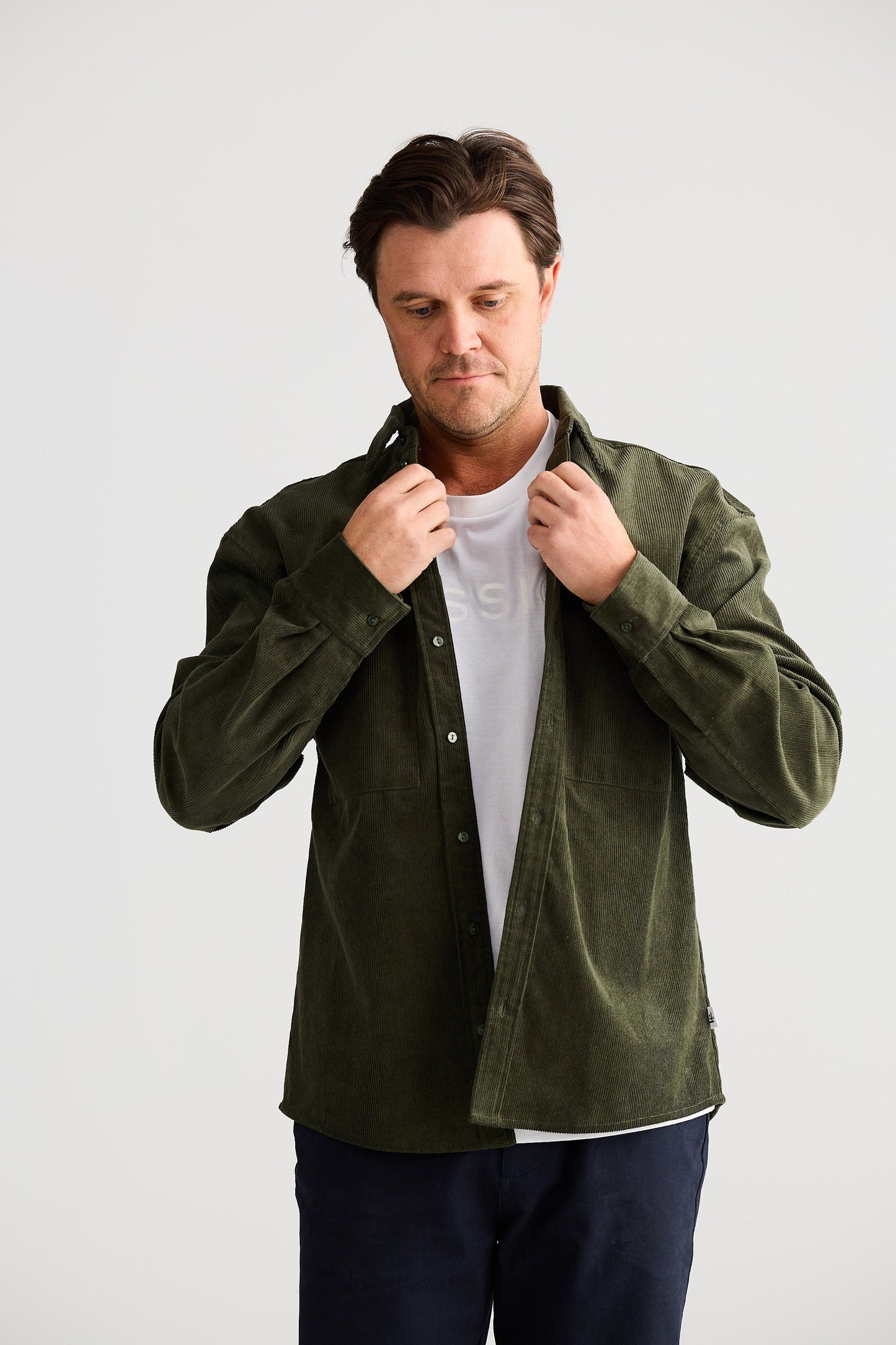 Man wearing a green jacket over a white shirt on a light gray background