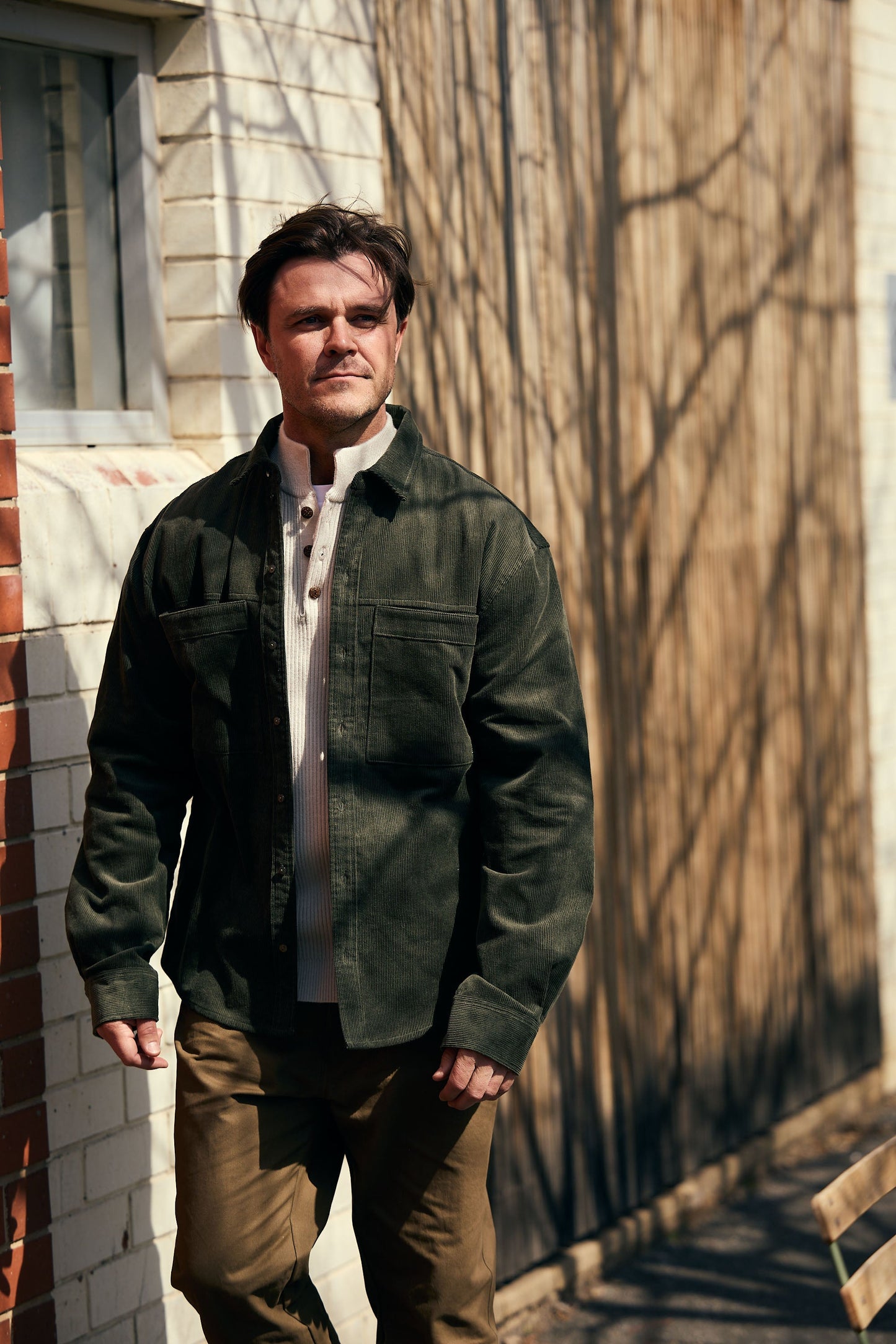 Man wearing a green jacket standing against a brick wall.