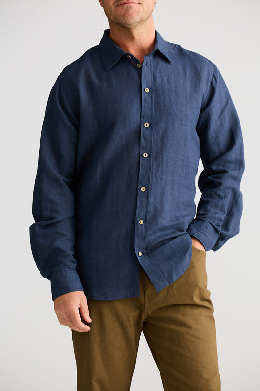 Man wearing a blue button-up shirt and brown pants on a white background