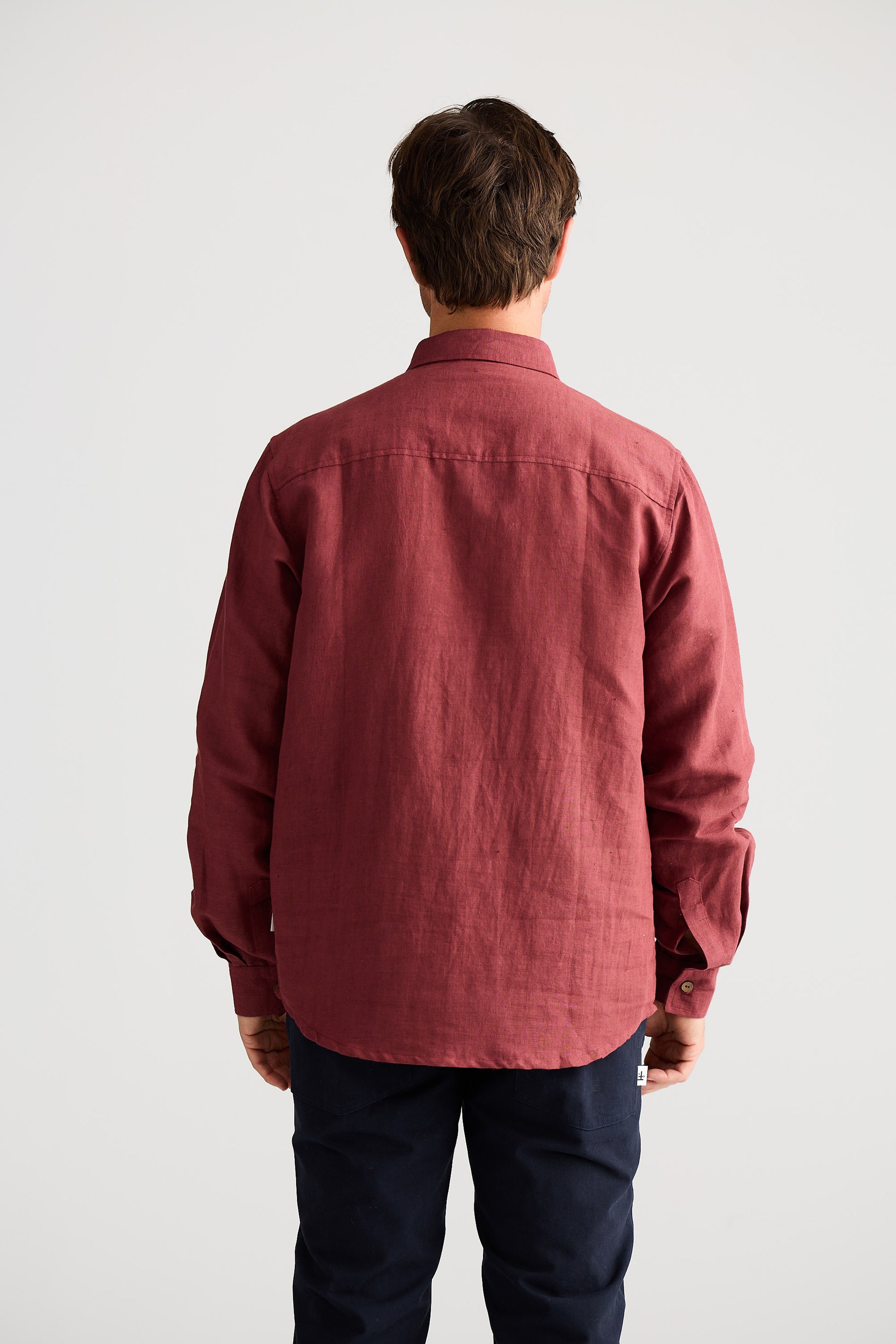 Man wearing a red shirt and dark pants against a white background