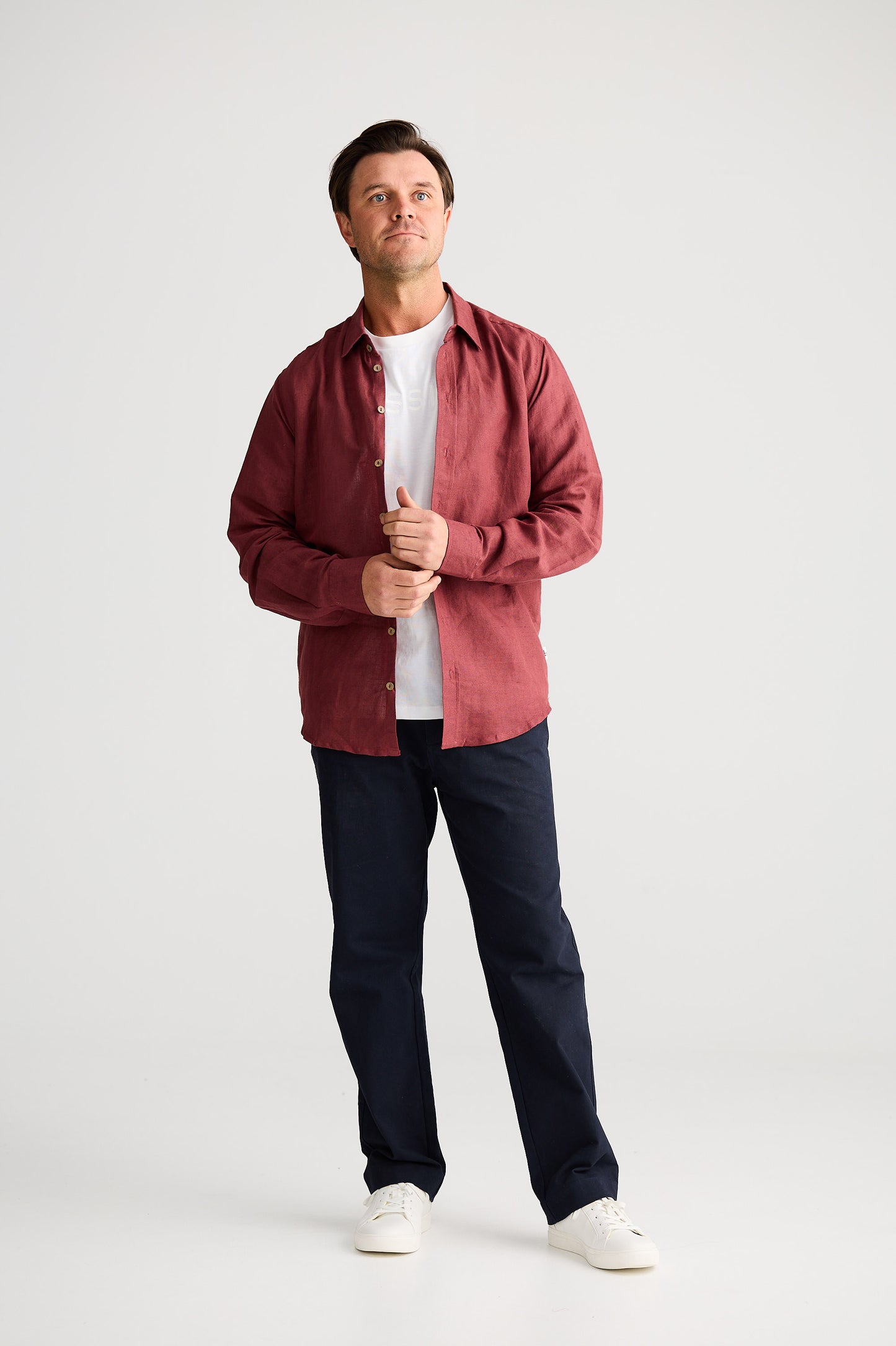 Man wearing a red shirt, white t-shirt, dark pants, and white shoes on a white background