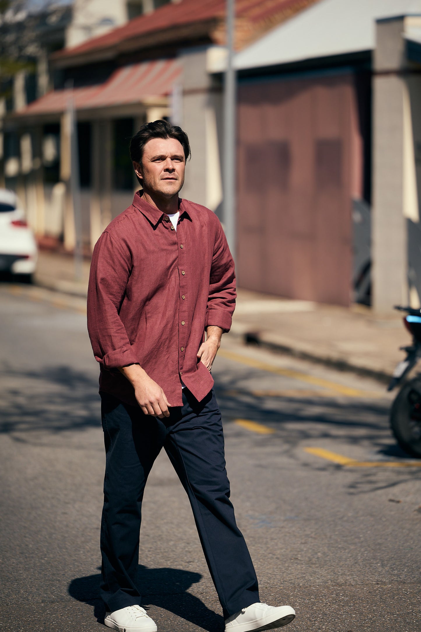 Man in a red shirt walking on a street with buildings in the background