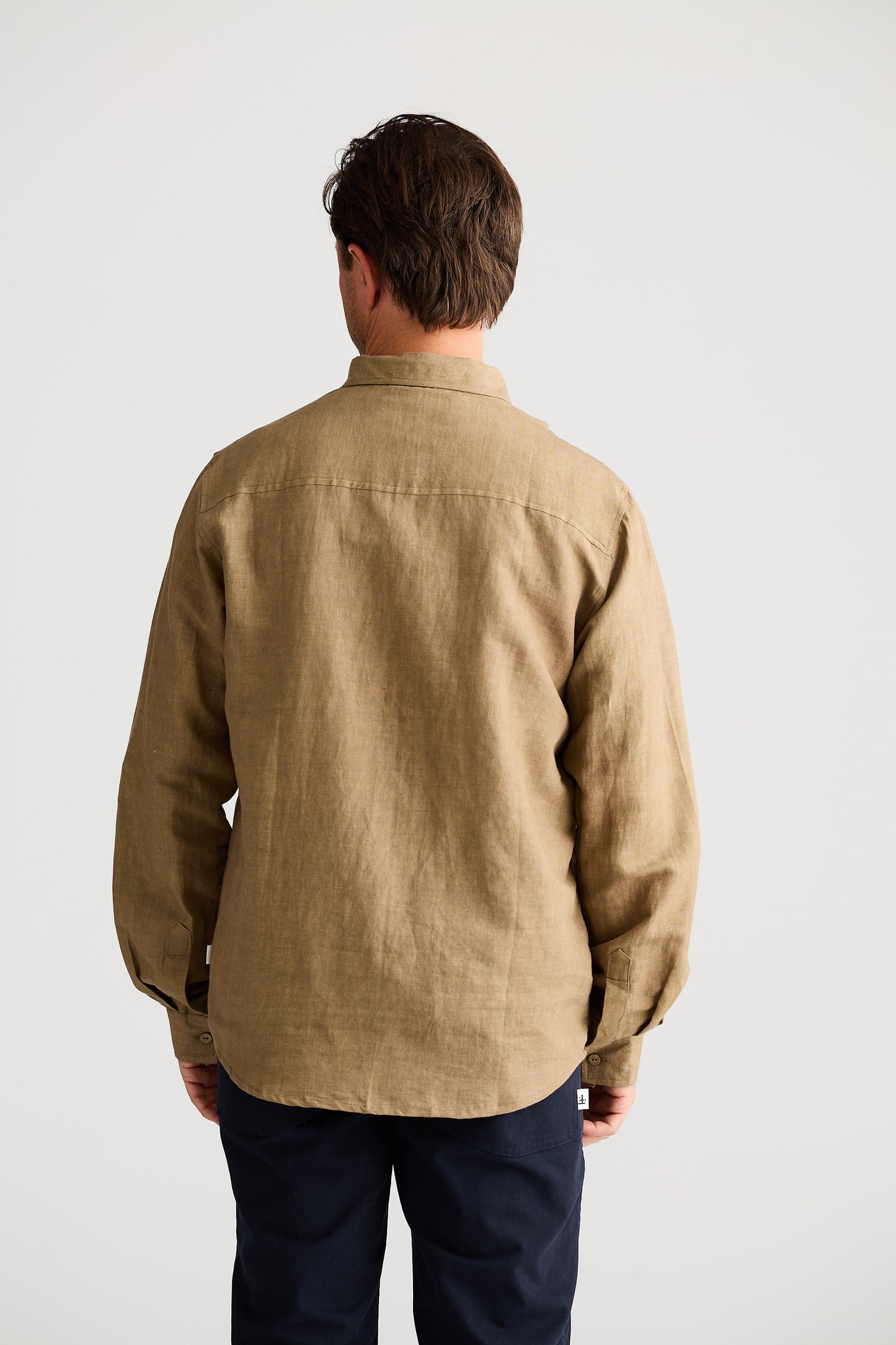 Man wearing a beige shirt and dark pants against a white background