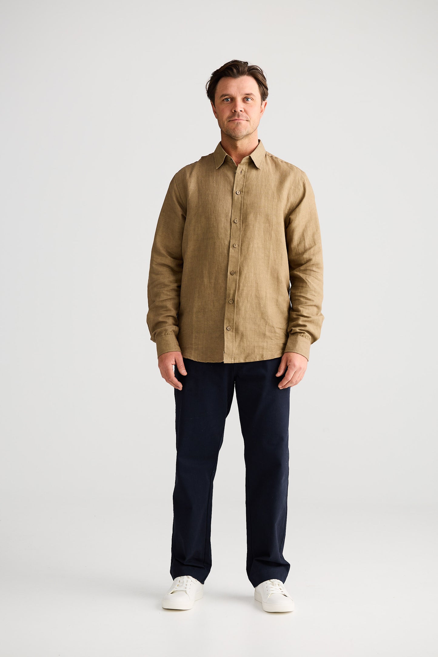 Man wearing a beige shirt and dark pants on a white background