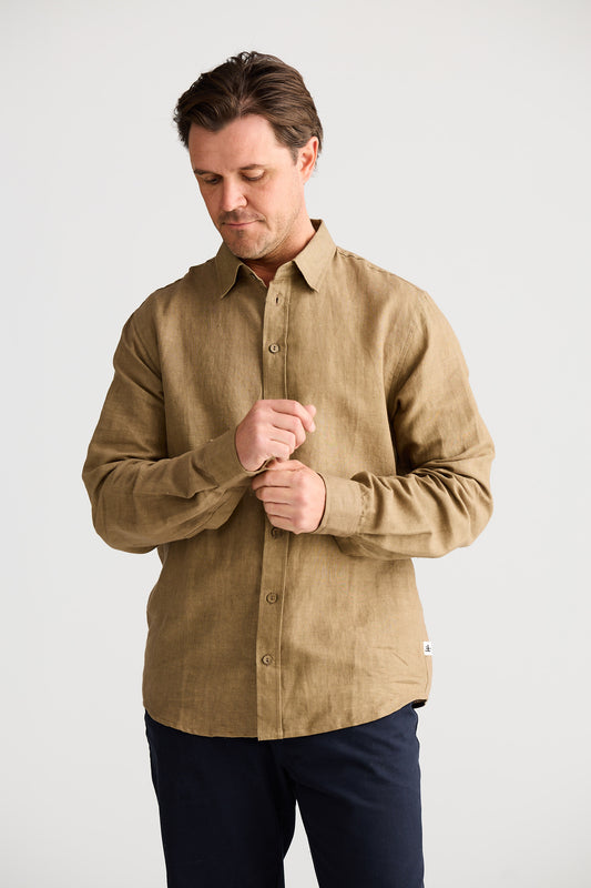 Man wearing a beige shirt and dark pants on a white background