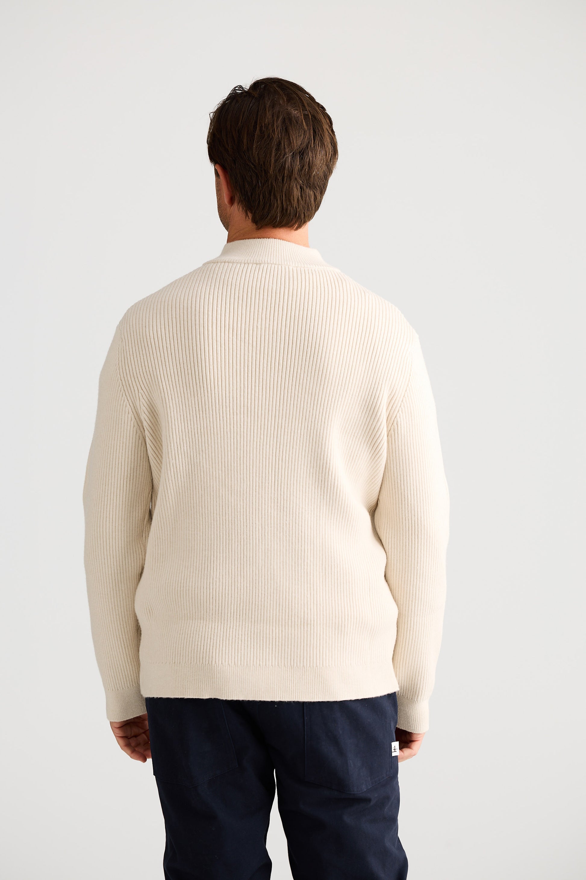 Man wearing a cream sweater and navy pants against a white background