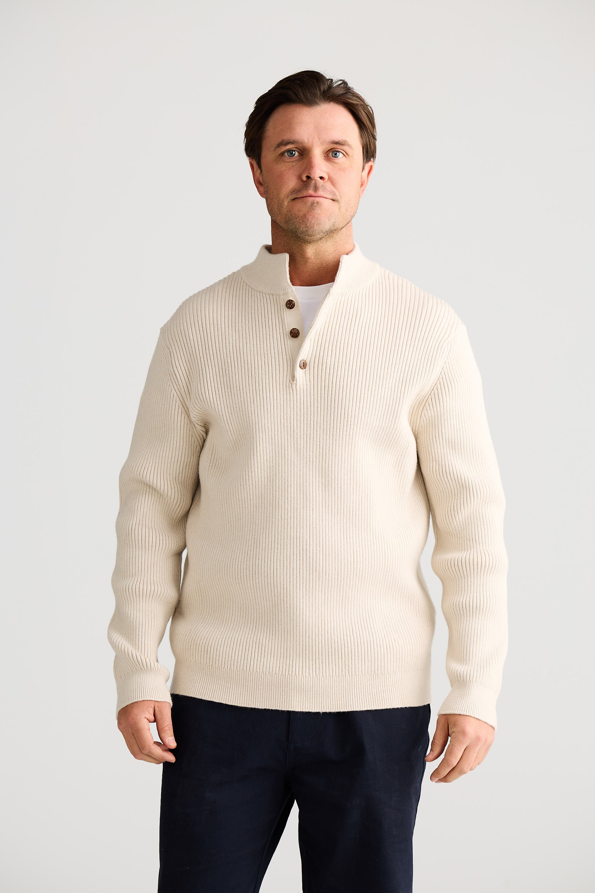 Man wearing a cream cardigan over a white shirt with navy pants on a light gray background