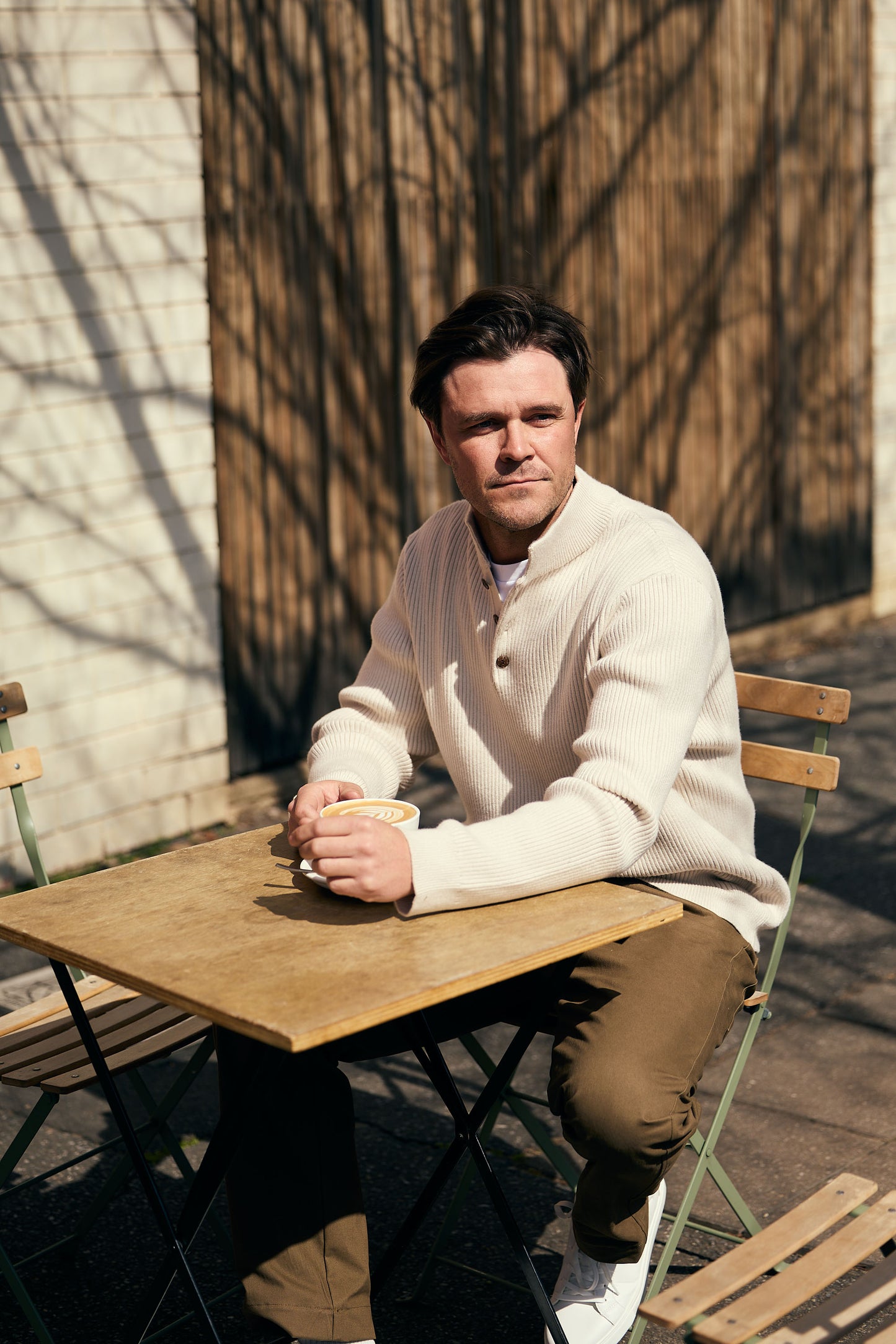 Man sitting at a wooden table outdoors holding a cup.