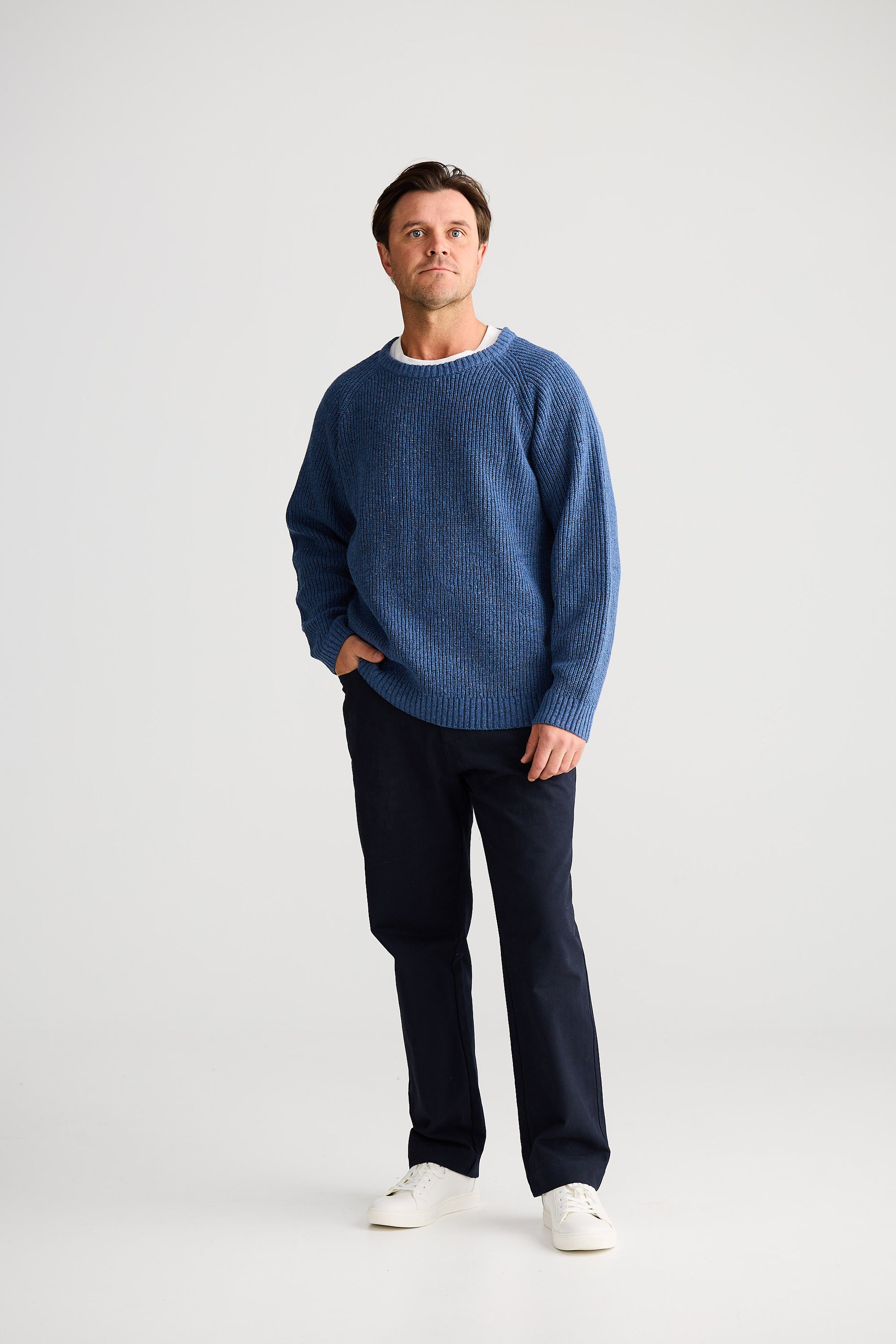 Man wearing a blue sweater and dark pants on a white background