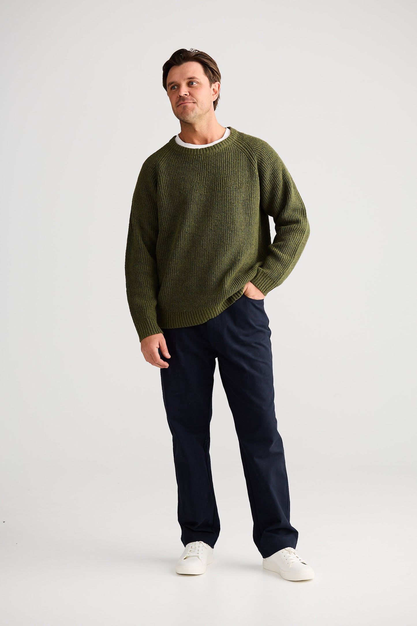 Man wearing a green sweater and dark pants on a white background