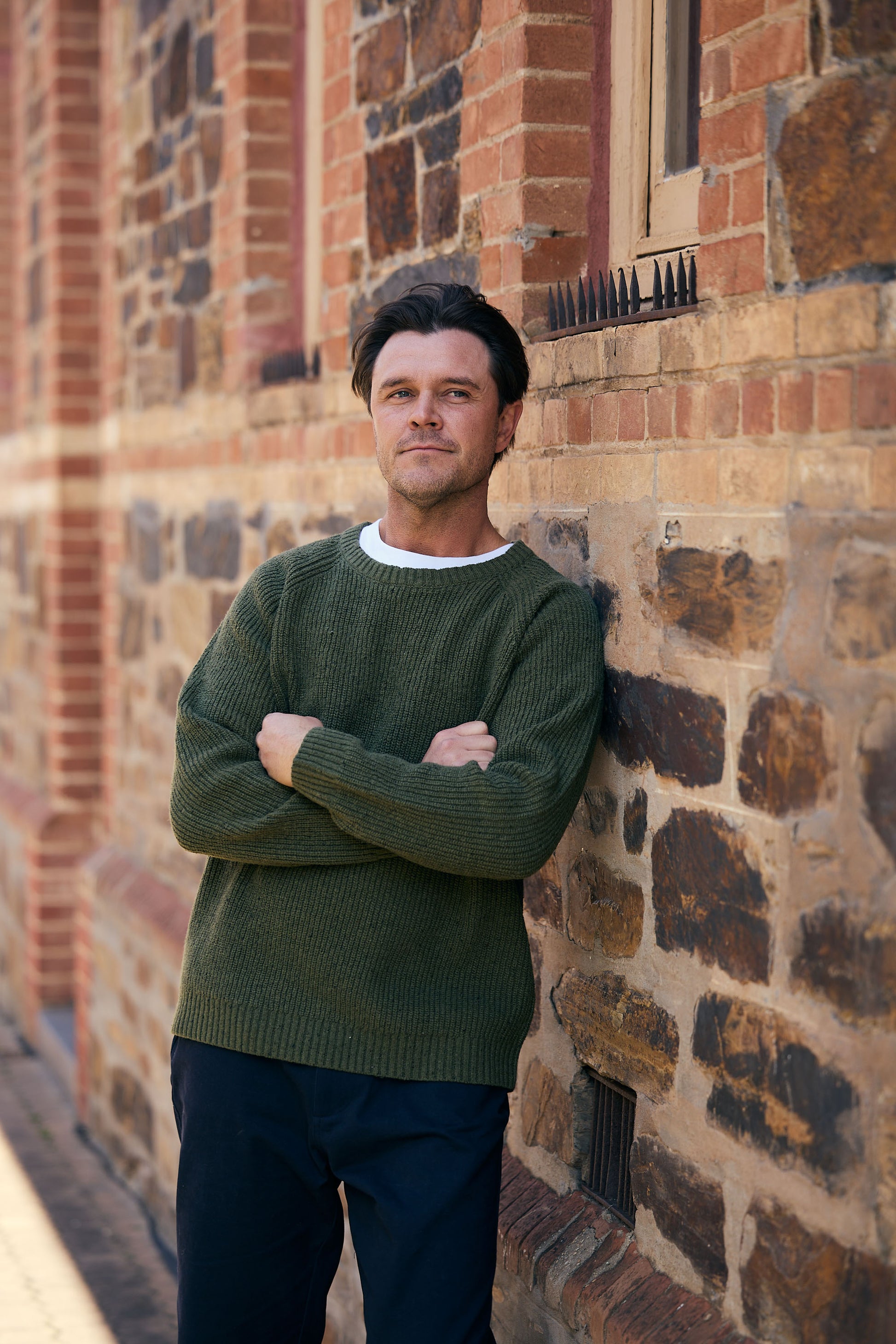 Man standing against a brick wall wearing a green sweater