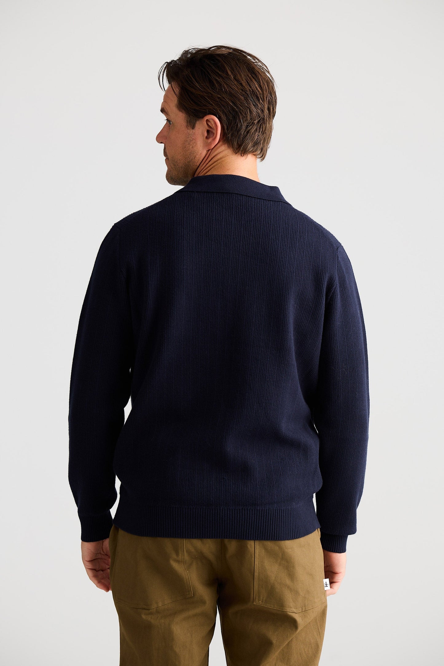 Man wearing a navy sweater and beige pants against a white background